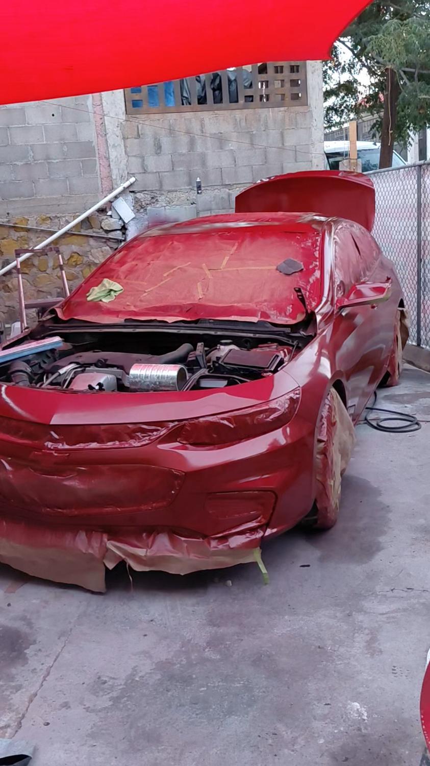 Sedán rojo en primario, con el cofre abierto